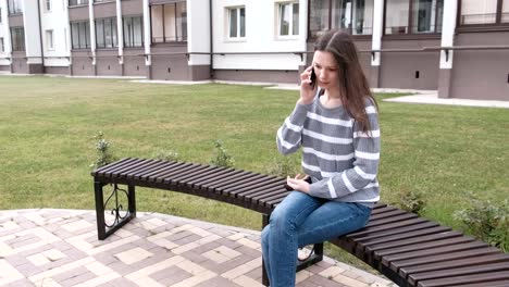 Woman-is-calling-mobile-phone-sitting-on-the-bench-near-the-house.