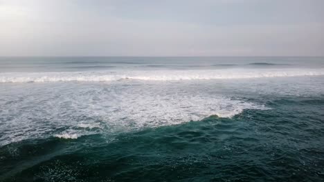 Drone-flying-above-small-boat-and-ocean-waves,-turning-back-to-reveal-magnificent-tropical-resort-house-on-the-shore