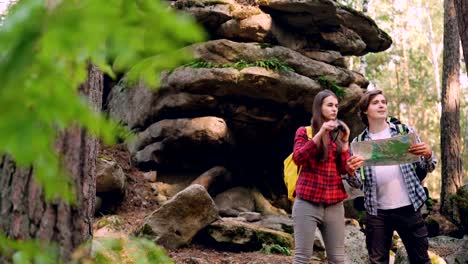 Turistas-perdidos-son-permanente-en-bosque-cerca-de-enormes-rocas,-busca-en-el-mapa-y-luego-a-través-de-binoculares-y-hablando-de-manera-discutir-a-su-lugar-de-destino.-Concepto-de-personas-y-la-naturaleza.