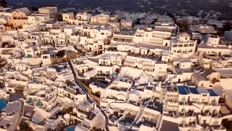 Flight-over-traditional-terraced-white-villas-in-Fira-(Thira)-town-at-sunset,-Santorini,-Greece