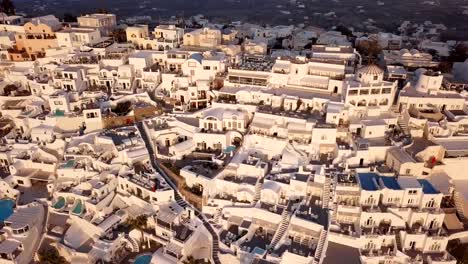 Vuelo-sobre-villas-blancas-terrazas-tradicionales-ciudad-de-Fira-(Thira)-al-atardecer,-Santorini,-Grecia