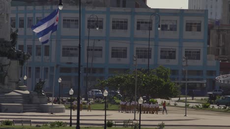 cuban-school-kids-in-everyday-life-in-old-Havana,-cuban-flag-on-public-square