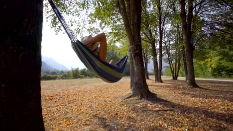 Glückliche-junge-Frau-in-Hängematte-schwingen-bei-Sonnenuntergang-Beine-Spaß-und-Freiheit-in-der-Natur---spät-Sommertage-zu-genießen.-Menschen-Freude-Reisekonzept