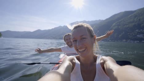 Junges-Paar-in-den-Sommerferien-Kanu-auf-dem-See-in-den-Bergen-zu-genießen.-Die-Leute-Reisen-Spaß-Urlaub-Konzept.-Technologie-und-Jugendkultur-nehmen-Selfie---4K