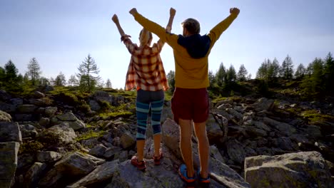 Junges-Paar-auf-einer-Wanderung-umgeben-von-Berggipfeln,-die-Arme-ausgestreckt-vor-der-Sonne,-Wandern,-Arme-weit-geöffnet-Freiheit-und-Erfolg-Konzept-paar-stehend