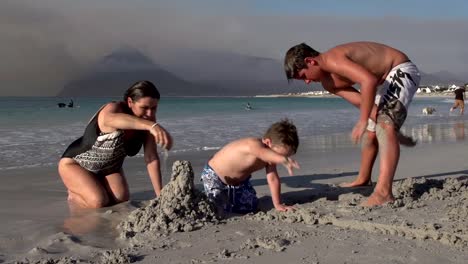 Madre-con-dos-niños-jugando-en-la-arena-en-la-playa,-Cape-Town