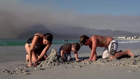 Mother-with-2-children-playing-with-sand-on-beach,-Cape-Town