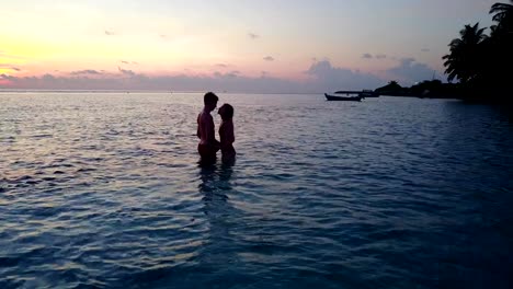 v04152-Aerial-flying-drone-view-of-Maldives-white-sandy-beach-2-people-young-couple-man-woman-romantic-love-sunset-sunrise-on-sunny-tropical-paradise-island-with-aqua-blue-sky-sea-water-ocean-4k
