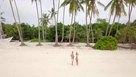 Young-couple-playing-with-drone,-waving-hands-to-the-flying-helicopter.-People-fun-new-technology-vacations-concept.-Shot-on-tropical-beach-in-the-Philippines,-4K-resolution