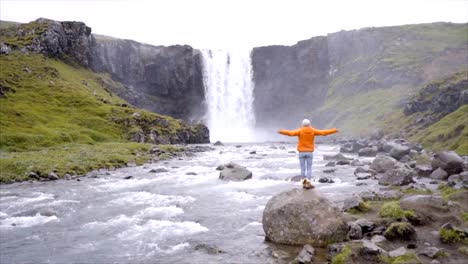 Young-woman-arms-outstretched-in-front-of-the-magnificent-waterfall-in-Iceland.-People-travel-exploration-concept--Slow-motion