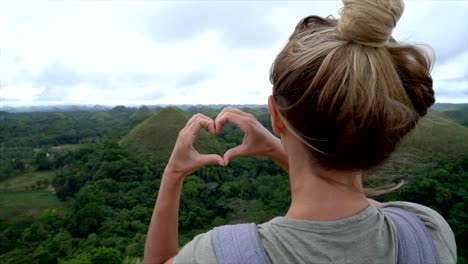 LENTA-de-chica-viajando-hace-el-corazón-en-las-colinas-de-Chocolate-de-Bohol,-Filipinas