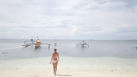 Drone-shot-aerial-view-of-young-woman-walking-on-idyllic-tropical-beach