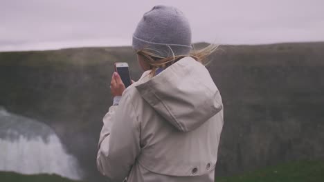 Joven-touristtaking-pucture-con-smartphone-de-cascada-en-Islandia,-cardán-tiros,-cámara-lenta