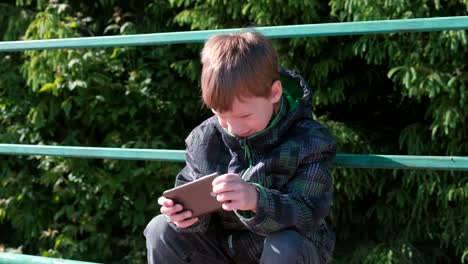 El-niño-juega-un-juego-en-su-teléfono-móvil-mientras-está-sentado-en-el-parque.