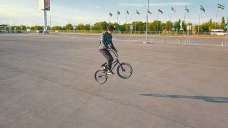 cámara-de-jinete-joven-adolescente-masculino-del-vuelo-en-la-bicicleta-de-bmx-en-el-lugar-vacío-urbano-que-nadie-de-asfalto