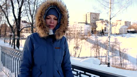 Mujer-joven-en-azul-por-la-chaqueta-con-capucha-de-piel-caminando-en-el-parque-de-invierno-y-congelamiento-en-la-calle.-Vista-frontal.