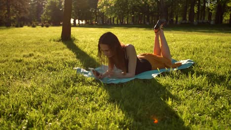 Mujer-establecen-sobre-hierba-verde-mientras-se-escribe-un-mensaje-en-el-teléfono