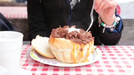 Niña-turismo-comer-un-estofado-en-un-tazón-de-pan-en-el-mercado-anual-de-Navidad-en-Budapest.-Turistas-disfrutando-y-degustación-de-cocina-tradicional-húngara