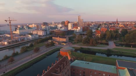 Aerial-view-flying-over-Malmo-cityscape-at-sunset.-Drone-shot-of-"Malmohus"-in-Sweden,-construction-site-and-city-in-the-background