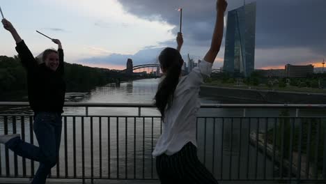 Young-Women-Having-Fun-With-Sparklers-on-City-Bridge