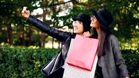 Adictos-de-alegres-señoritas-toman-selfie-en-la-calle-sosteniendo-bolsas-y-haciendo-muecas.-Las-mujeres-están-usando-gafas-y-prendas-de-vestir-con-estilo.