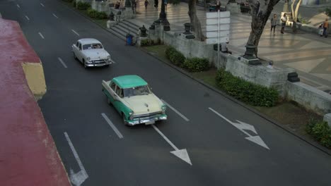 Rooftop-view-on-classic-american-cars-driving-on-a-street-in-Havana,-Cuba