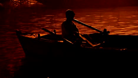 Junge-in-einem-Boot,-beleuchtet-von-der-Ghats-am-Ganges:--Varanasi,-Indien