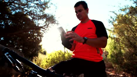 Mountain-biker-sitting-on-bike-looking-at-his-smart-phone