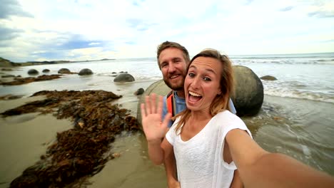 Young-couple-stand-near-Moeraki-boulders-and-take-selfie-portrait