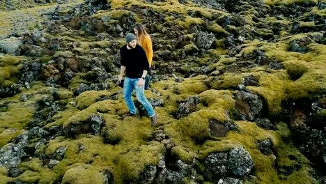 Vista-aérea-de-la-joven-pareja-elegante-paseando-por-el-campo-de-lava-volcánica-en-Islandia.-Hombre-y-la-mujer-van-a-su-coche