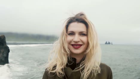 Young-happy-woman-standing-on-black-beach,-near-the-troll-toes-rocks-and-having-fun.-Kissing-camera-and-smiling