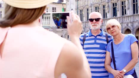 Daughter-taking-photo-of-her-senior-parents-on-vacation-trip-in-central-square-of-Brussels,-Belgium