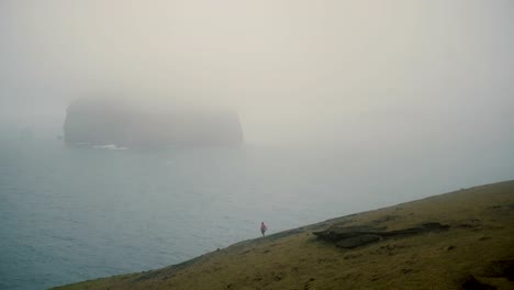 Young-traveler-walking-on-the-shore-of-the-sea-in-fog-and-exploring-beach-in-overcast-day-in-Iceland-near-Vestmannaeyjar