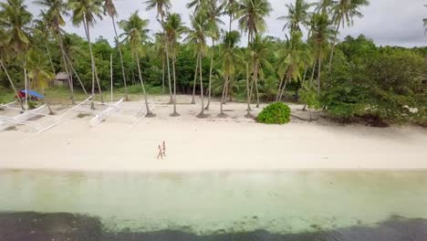 Drone-shot-aerial-view-of-young-couple-walking-on-tropical-beach-in-the-Philippines.-Palm-trees-and-clear-blue-water.-People-travel-love-romance-vacations-concept.-4K-resolution-video