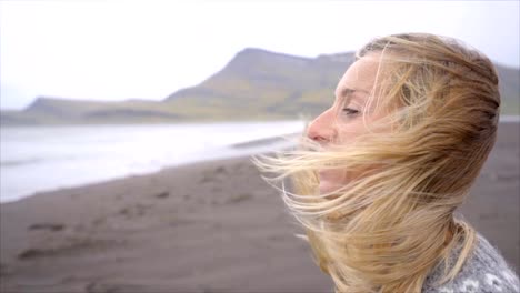 Junge-Frau-Betrachtung-stehenden-Meer-am-schwarzen-Sandstrand,-Haare-im-Wind-Island-Slow-Motion-Video-Menschen-reisen-Natur-Konzept