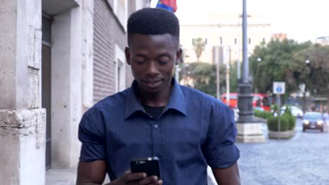Porträt-von-attraktiven-schwarzen-afrikanischen-Mann-zu-Fuß-in-die-Stadt,-tippen-auf-seinem-smartphone