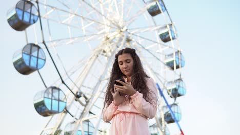 Das-Mädchen-ist-einen-Smartphone-Stand-in-der-Nähe-das-Riesenrad.4K-verwenden.