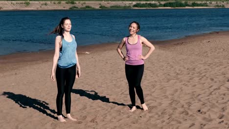 Two-woman-doing-stretching-after-jogging-along-the-sandy-beach-of-the-river-at-sunset.