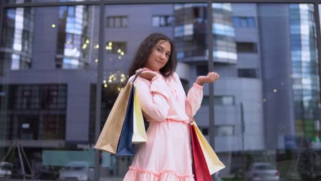 Chica-joven-en-un-vestido-después-de-compras-posando-con-paquetes-en-las-manos.-4K