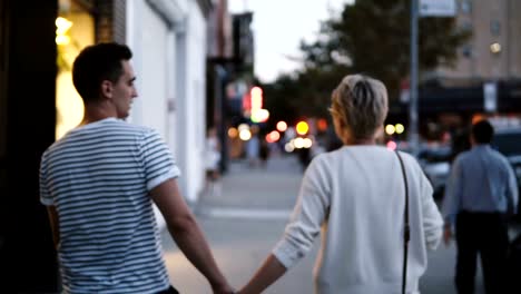 Happy-young-romantic-couple-hold-hands-walking-along-evening-Soho,-New-York,-blurred-street-lights-in-the-background