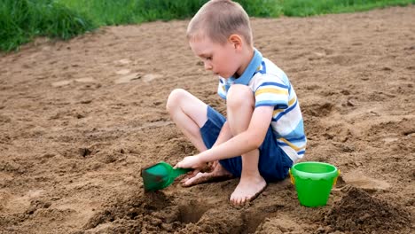 Schwere-kleine-Junge-gräbt-eine-Grube-mit-einer-Schaufel.-Kinder-spielen-am-Strand