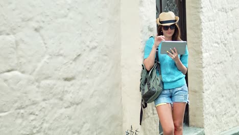 Atractivos-turísticos-mujer-de-pie-junto-a-la-antigua-pared-tocando-la-pantalla-del-tablet-PC-en-el-día-de-verano