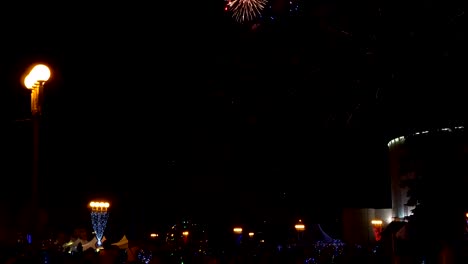 People-stand-on-the-square-and-watch-the-fireworks-above-the-city-in-the-night-sky-against-the-buildings.-Fireworks-show.