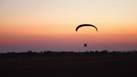 The-pilot-on-a-paraglider-flies-in-the-sky-after-sunset-with-orange-.-background