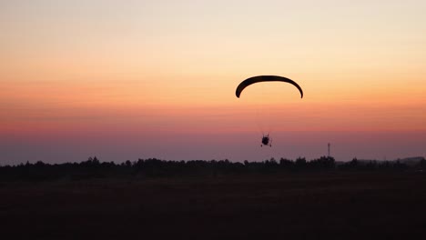 Der-Pilot-auf-einem-Gleitschirm-fliegt-in-den-Himmel-nach-Sonnenuntergang-mit-Orange.-Hintergrund