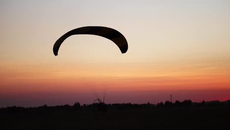 El-piloto-en-el-parapente-viene-a-la-tierra-en-el-campo-al-atardecer