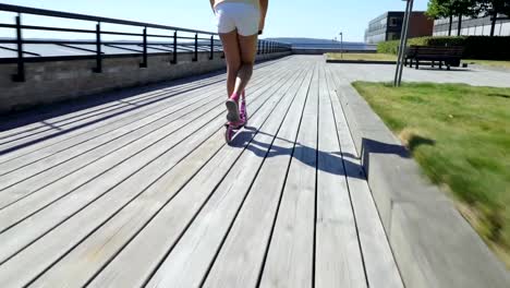 Teenager-Mädchen-Reiten-ein-Kick-Scooter-auf-der-hölzernen-Strandpromenade.