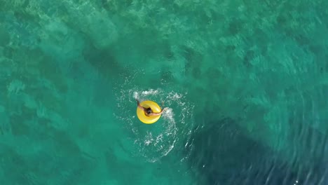 Aerial-view-of-woman-spinning-with-inflatable-on-Atokos-island,-Greece.