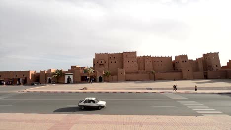 People-walking-and-cars-passing-by-in-front-of-the-outer-walls-of-the-front-façade-of-Kasbah-Taourirt