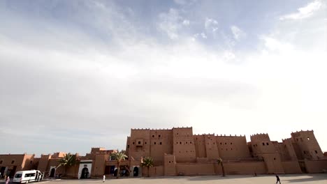 People-walking-and-cars-passing-by-in-front-of-the-outer-walls-of-the-front-façade-of-Kasbah-Taourirt